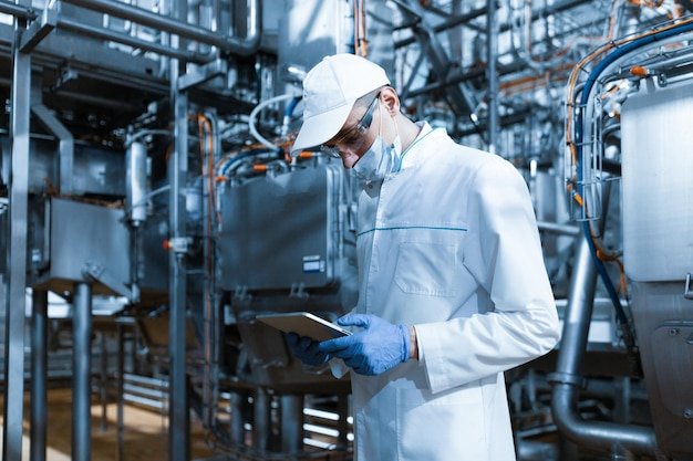 concentrated-technologist-taking-necessary-notes-with-help-digital-tablet-while-standing-production-department-dairy-factory-inspector-carries-out-control-cheese-factory_645730-70